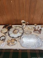 Full image of the lot on table showing all items including trays, cups, candlesticks, pitcher, and tea set components.