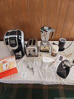 Wide shot showing assortment of small kitchen appliances including Keurig coffee maker, Osterizer blender, stainless steel toaster, various small kitchen utensils, and boxes.
