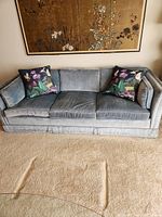 Front view of blue velvet sofa with two floral pillows and artwork above.