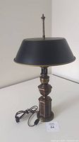 Full view of the vintage resin and metal table lamp with black shade and cord with inline switch placed on a white surface against a white wall.