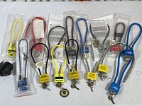 Full lot of 12 child safety trigger locks, mostly new and in packaging, with various colors including yellow, black, red, blue, and gray, each with keyed locks and flexible cable loops or plastic handles.