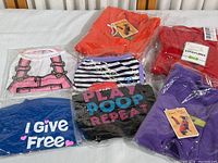 Seven new medium dog clothes arranged on a surface showing variety of shirts and jackets in original packaging.
