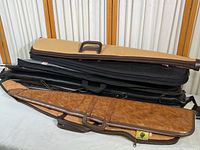 Nine rifle cases stacked, showing different materials and colors including tan, brown leather, and black cases.