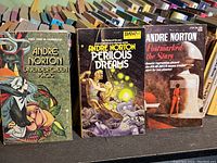 Close-up of three Andre Norton books with visible cover art and titles: Lavender-Green Magic, Perilous Dreams, Postmarked the Stars