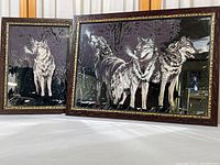 Pair of framed mirrored wolf prints with one showing single wolf howling and the other showing three wolves standing.