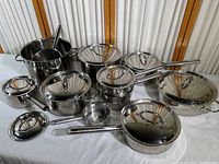 Full assortment of stainless steel cookware, lids and ladle arranged on cloth