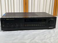 Front view of Sherwood RA-1145R stereo receiver showing main power switch, speaker selector, headphone jack, and bass, treble, balance adjustment knobs along with alphanumeric display and multiple channel control buttons.