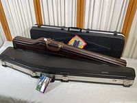 Photo showing three black hard rifle cases stacked. Cases are new, two have tags visible. One case shows SKB brand and size measurement.