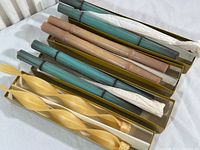 Four pairs of long beeswax candles displayed in boxes on a flat surface, including one twist and three bamboo design pairs.