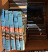 Photo shows a close-up of several Hardy Boys hardcover books arranged vertically in a box, displaying spines with titles, series branding, and author name.