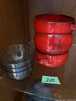 Stacked view of three red ceramic bowls and three clear glass bowls on a glass shelf