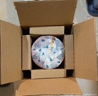 Top view showing the candle wrapped in original branded pink paper sitting inside a cardboard box with protective inserts.