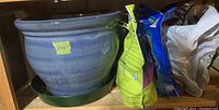 Large blue glazed ceramic pot next to gardening materials and smaller pot on shelf