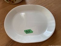 Close-up of a single white rectangular Corning Ware serving plate with a green sticker '405' on it, placed on wooden surface.