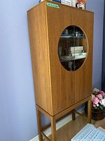 Front view of the wooden curio cabinet showing circular glass panels on double doors, standing on tall wooden legs.