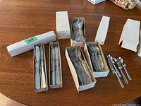 Full view of all cutlery items mostly in white original boxes on wood table.