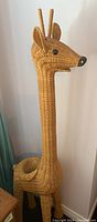 Full view of woven wicker giraffe shaped plant stand with long neck and ears, black nose and eyes