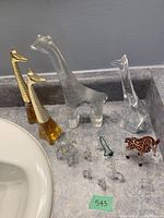 Photo showing twelve giraffe figurines of varying sizes and materials arranged on a countertop next to a sink basin.