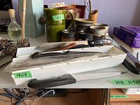 Lot of assorted kitchen knives arranged on trays showing different blade types and handles including wooden and black synthetic handles.