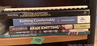 Photo of five books stacked on a shelf showing titles and authors: Merese Stanley, Carson Demers, Alice Starmore. Books include topics on knitting design, ergonomics, aran knitting, and Celtic knitting.