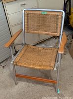 Front view of vintage folding lawn chair showing aluminum frame, wicker seat and backrest, wooden armrests.