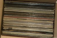 Top view showing about 30 stacked vinyl LP records in paper sleeves inside a cardboard box.
