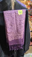 Full view of folded purple scarf hanging on display rack, showing lace floral pattern and tassels at end.