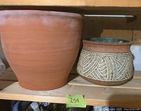 Side view of large terracotta pot and medium decorative clay pot on shelf