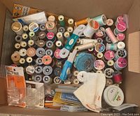 Overhead photo of a box filled with many spools of thread in different colors and materials, along with some packaged sewing supplies.