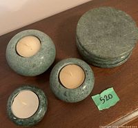 Photo showing three rounded stone tealight candleholders and stack of four round stone coasters, all green with natural veining.