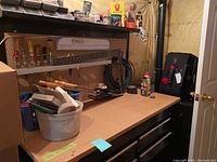 View of black tool bench with wooden work surface and pegboard back holding metal shelf with jars and hand tools.