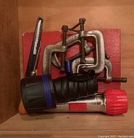 3 metal C-clamps, flashlight, and utility knife placed on wooden surface