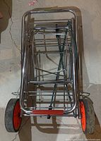 Top view of trolley cart folded flat showing metal frame and red wheels.