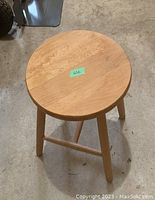 Photo showing the stool from a side angle, displaying the round seat, four legs, and cross supports.