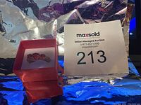 Front view of the ring showing the cluster of red stones set in a gold-tone frame inside a red box.