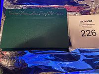 Closed green leather-like folder stamped 'United States Mint Proof Set 1996' with auction lot number on the side.