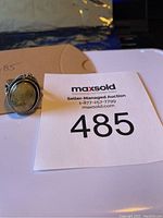 Photo front view of the sterling silver ring with oval green stone on a white surface with auction lot number 485 card.