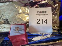 Image of the silver ring displayed in a red velvet box on a reflective surface with auction lot number card 214 visible.