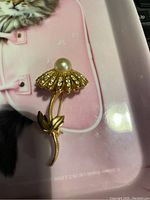 Top view of the flower brooch showing the pearl center and rhinestone petals on a gold-tone stem with leaves.