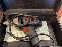 Vintage Sears Craftsman electric drill with power cord resting inside the open carrying case with paperwork underneath the drill.