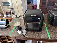 Front view of black Kalorik air fryer oven on countertop with power cord visible to the side.