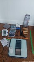 Overall view of all items showing the blood pressure monitor, chest strap, supports, wooden massage tools, and scale with manuals and packaging.