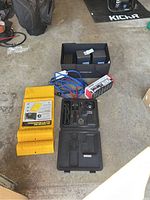 Photo showing various car accessories including a black air compressor in case, jumper cables, yellow parking mats and boxed Porsche mugs.