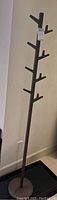 Photo of a tall dark brown wooden coat rack designed like a tree with multiple branched hooks against a wall and tile floor.