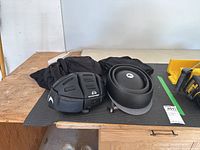 Four collapsible helmets shown on a black protective mat on a workbench: three rectangular-segmented black Morpher helmets and one smooth black Closca helmet in folded form.