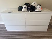 Front view of white dresser with six drawers and caps on top