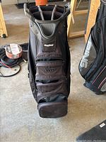 Front view of black BagBoy golf bag standing upright showing multiple zippered pockets and padded handle.
