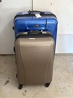 Photo showing front view of large blue and medium bronze hard shell luggage bags side by side on floor.