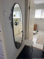 Full view of oval mirror hung on wall with side table placed in front of it in hallway corner.