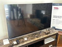 Front view of TV on stand with original box, HDMI cable, remote and stand feet pieces